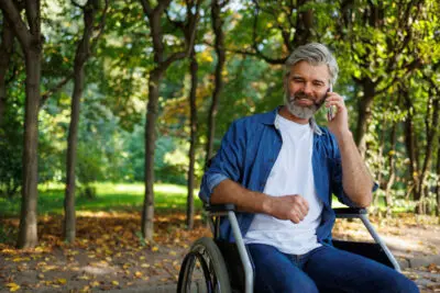 Man On The Phone Smiling In A Wheelchair In A Park