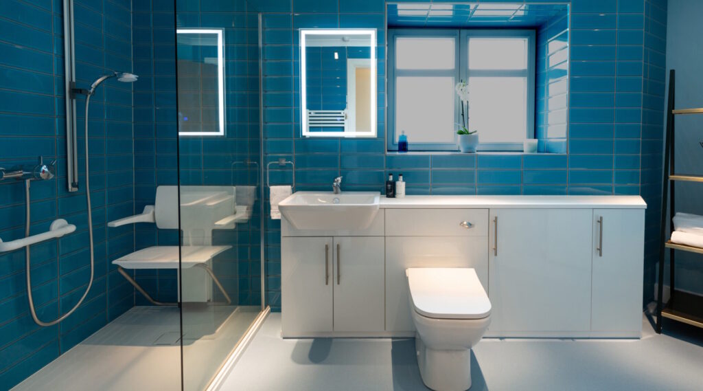 Photo of a luxurious walk-in shower featuring level-access tray folding seat with turquoise metro tiles and integrated comfort height toilet and sink