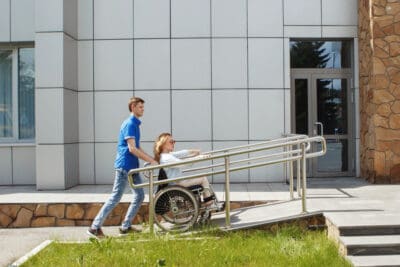 Man pushing woman in wheelchair up ramp to access a venue