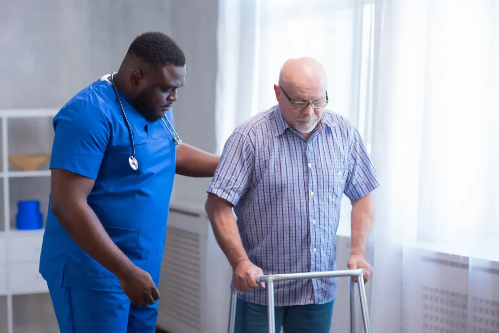 Caregiver Is Teaching Old Man To Walk With Walker.