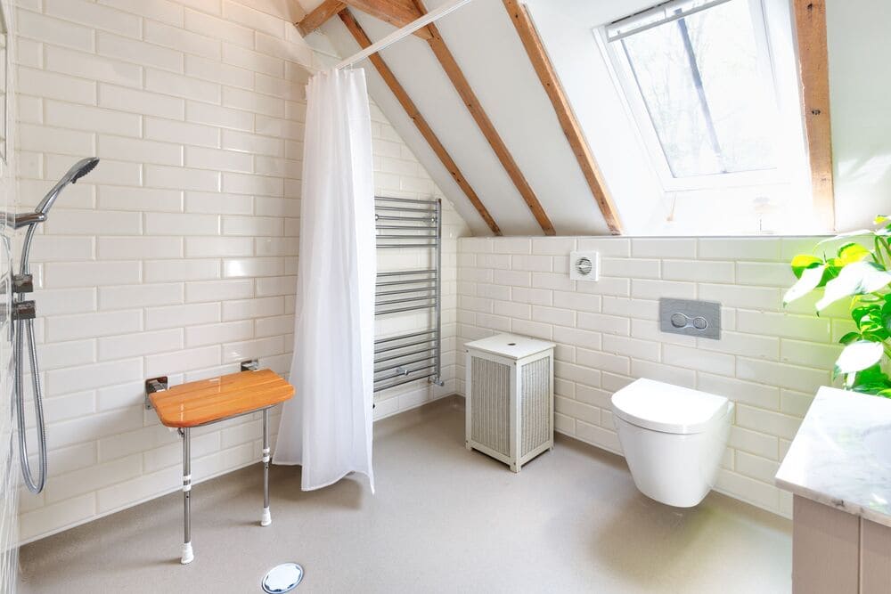 Mr And Mrs W's Bathroom After Renovation Walk In Shower With Shower Seat, Shower Curtain, Towel Rail, Small Laundry Basket And Toilet In A Bright, White Rom With Slanted Roof (1)