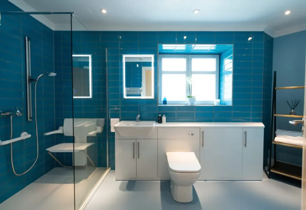 Mrs W's Bathroom After Renovation Blue Modern Tiling, And A Walk In Shower With Adjustable Seat, Grab Rails And Low Level Access. A New Toilet With White Modern Cabinet And Sink