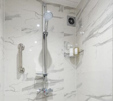 A vertical grabrail placed on the wall next to a shower with marbled wall panelling.