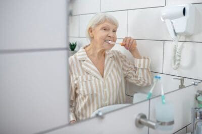 Elderly woman brushing her teeth in the mirror